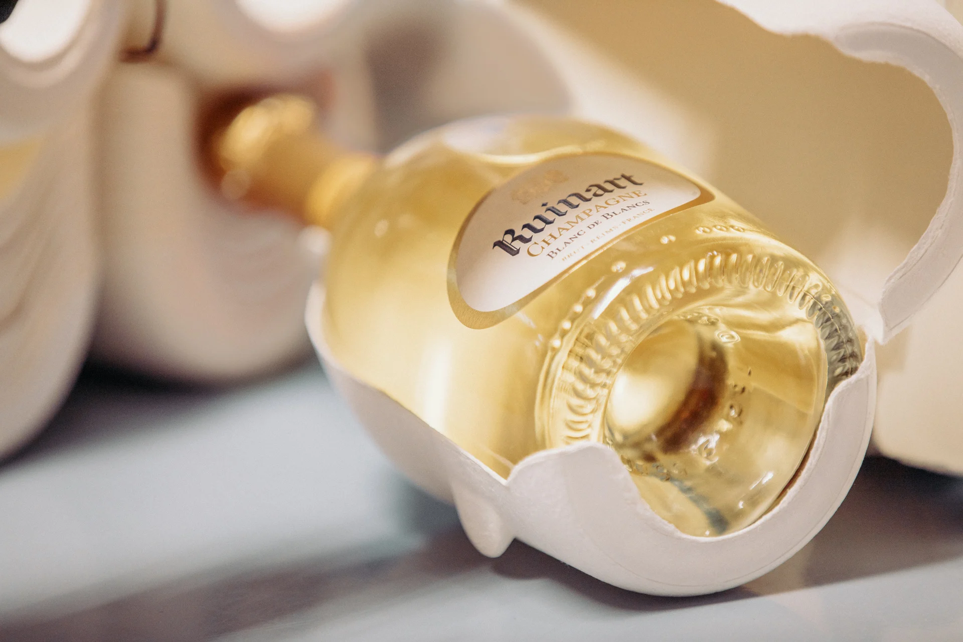 Champagne Ruinart Blanc de Blancs Seconde Peau, bouteille dorée aux reflets lumineux dans son écrin écologique en papier moulé.